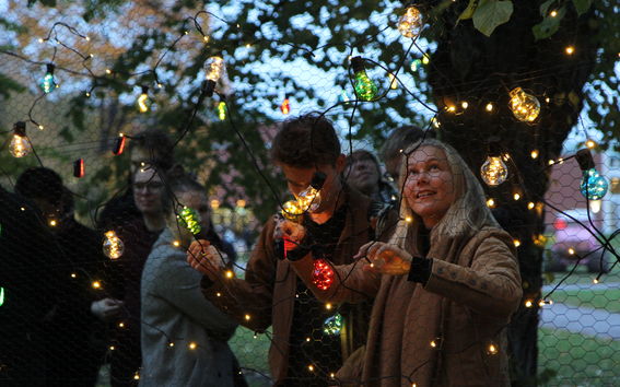 Nainen ripustaa valoketjua kanaverkkoaitaan ulkona