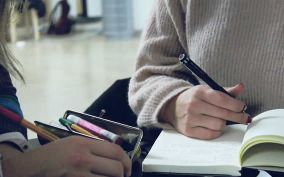 Two hands pictured writing in notebooks. 
