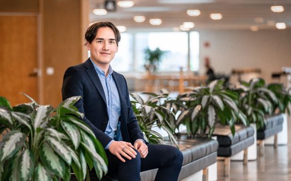 A man sitting on the sofa wearing a black suit and smiling for the camera.