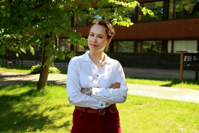 Picture of a person standing in front of a tree, smiling slightly with crossed arms.