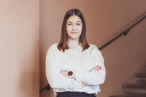 Nuori nainen seisoo kädet puuskassa, positiivinen ilme