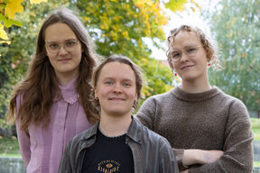 Three people smiling in front of an autumn background.