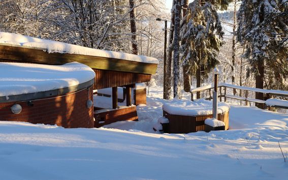 Rantasauna and hot tub covered in snow in winter sun.