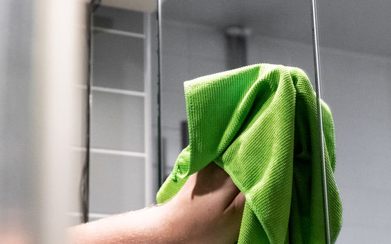 A hand cleaning a mirror with a green cloth.
