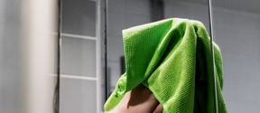 A hand cleaning a mirror with a green cloth.