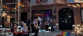 People sitting in front of a bar named The Stonewall Inn, decorated with rainbows