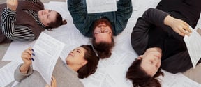 Four students laying on top of white paper and reading