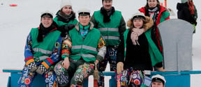 Seitsemän haalareihin ja vihreään liiviin pukeutunutta opiskelijaa Ullanlinnanmäellä vasaran muotoisen mäenlaskuvälineen edessä.