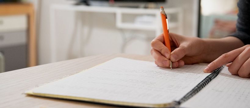 Person's hands writing notes on a notebook with a pencil