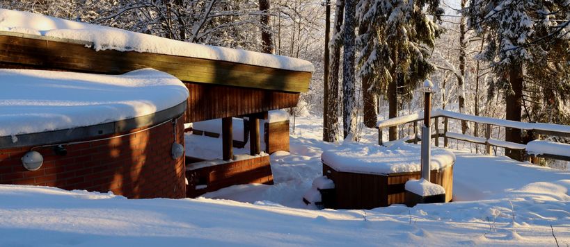 Rantasauna and hot tub covered in snow in winter sun.