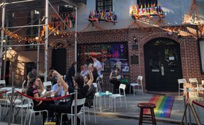 People sitting in front of a bar named The Stonewall Inn, decorated with rainbows